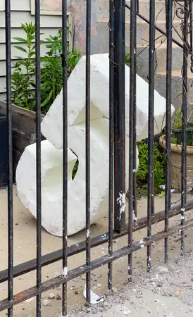 a large styrofoam number 5 that is tilted at an angle resting against and behind a metal fence in front of an apartment building