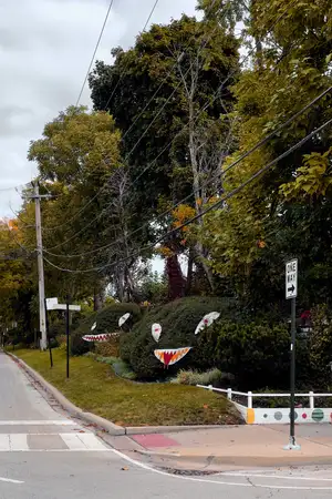 Two large bushes on the side of a road have large textile decals of eyes and mouths with pointy