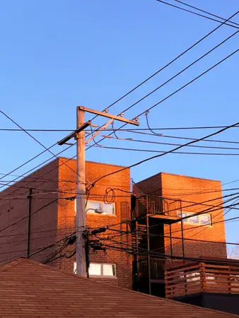 a typical Chicago apartment building with the wooden staircase in the back is basked in the evening sun. In the foreground a power pole stands with electrical wires running off of it in all directions
